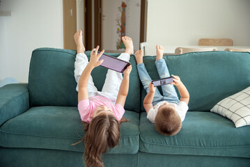 kids lie on the sofa in the living room, looking at the tablet. Making parent call, playing video...