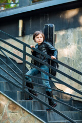 A beautiful, sweet girl standing on the stairs in jeans and a leather jacket, with an acoustic guitar in a case