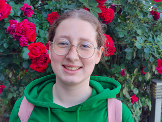 Cheerful Person Wearing Glasses Smiling in Front of Red Flowers in Garden or Park Setting