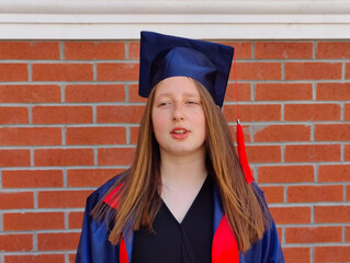 The image shows a young adult wearing a blue graduation cap and gown, indicating recent graduation...