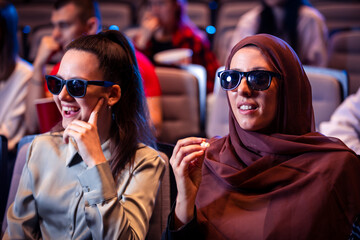Hijab muslim woman watching a 3d movie in cinema with her friends. Eating popcorn and enjoying.