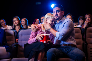 Couple watching horror movie, girlfriend is scared and her boyfriend is hugging her. Eating popcorn.