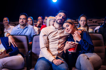 Young couple watching a movie in cinema. Hugging and eating popcorn.