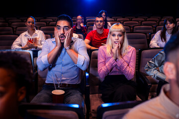 People watching horror movie in cinema. They are scared.