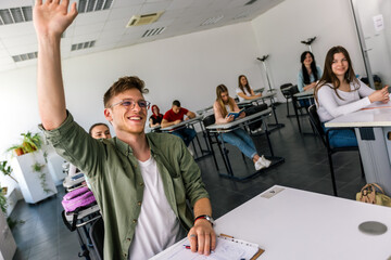 Male student raising his hand in class to ask some question.