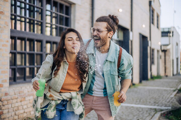 Young laughing hipster couple standing on street and spilling juice.