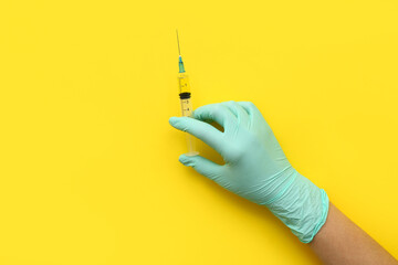 Female doctor with medical syringe on yellow background