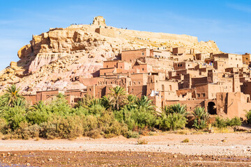 View of Ksar Ait Ben Haddou, old Berber adobe-brick village or kasbah in green oasis with palm...