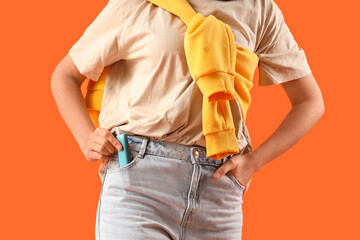 Young woman with electronic cigar in jeans pocket on orange background, closeup