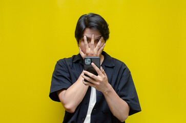 young asian man shocked covering his face after receiving unwanted news from his phone. asian man...