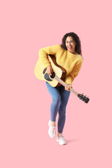 Young African-American woman playing acoustic guitar on pink background