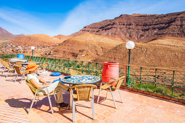 Young woman tourist sitting on restaurant terrace and looking at Atlas mountains on route to Tizi...