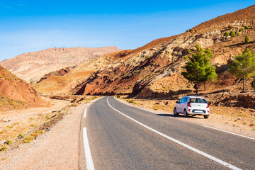 Rental car parking near paved asphalt road in Atlas mountains with high peaks and desert arid...