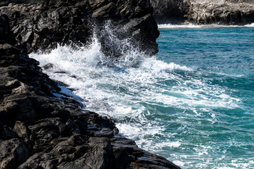 Rocky seascape and blue Pacific Ocean, waves crashing on lava rock, as a nature background
