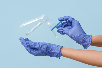 Doctor hands in medical gloves with gynecological speculum on blue background
