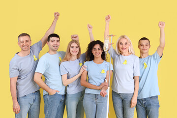 Obraz premium Young woman undergoing chemical therapy course and people with yellow awareness ribbons on color background. World Cancer Day