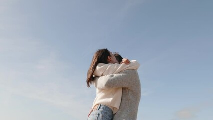 A touching moment as a couple embraces for what seems like the last time, set against a clear sky.