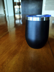 Black thermos cup on the wooden table.

