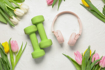 Composition with dumbbells, headphones and beautiful tulip flowers on light background