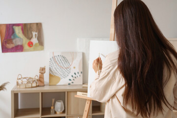 Female artist drawing on easel at home, back view