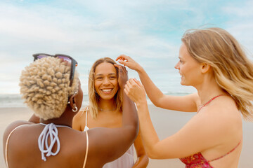 two girls combing a friend's hair on the beach during a summer trip. Friendship and unity.