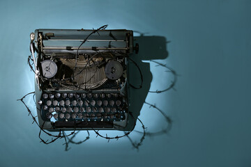 Vintage typewriter with barbed wire on blue background. Printing ban concept