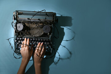 Female hands with vintage typewriter and barbed wire on blue background. Printing ban concept