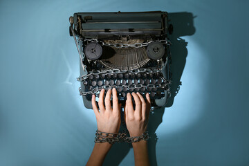 Female hands with vintage typewriter and chains on blue background. Printing ban concept