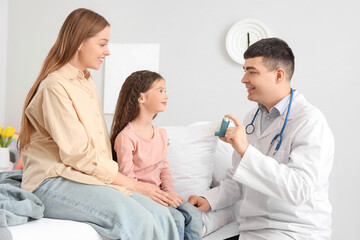 Obraz premium Male pediatrician showing inhaler to little girl and her mother in bedroom