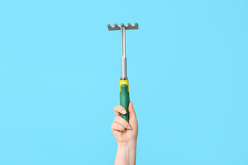 Female hand with gardening rake on color background, closeup