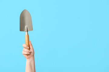 Female hand with gardening shovel on color background, closeup