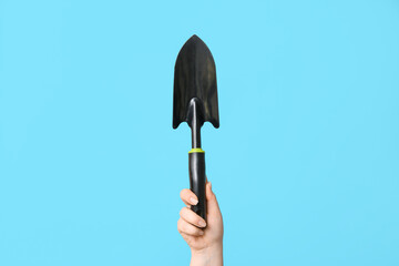 Female hand with gardening shovel on color background, closeup
