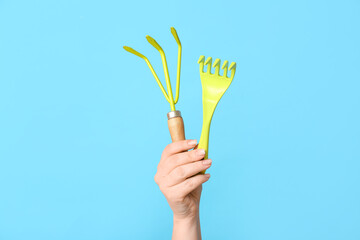 Female hand with gardening rakes on color background, closeup