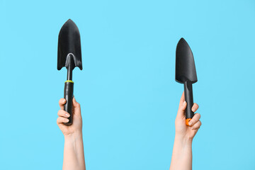 Female hands with gardening shovels on color background, closeup