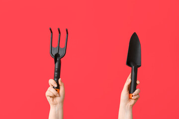 Female hands with gardening rake and shovel on red background, closeup