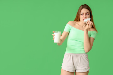 Woman with glass of milk and tissue suffering from allergy on green background