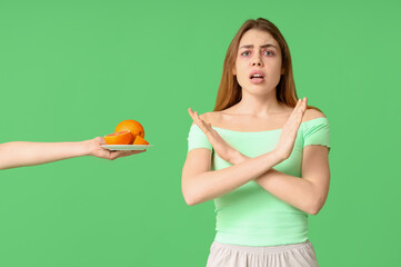 Woman showing STOP gesture and female hand with grapefruit on green background