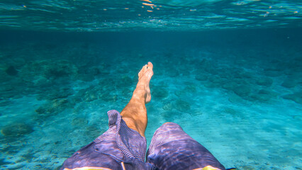 POV UNDERWATER: Male person swimming alone in crystal clear turquoise Adriatic Sea. Unrecognizable...