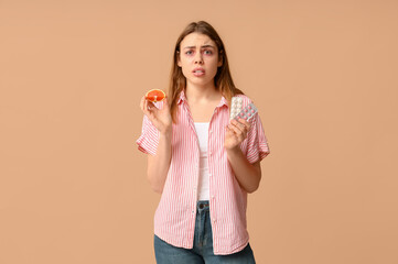 Young woman with grapefruit and pills suffering from allergy on brown background