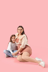 Little girl with her pregnant mother hugging on pink background