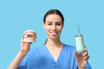 Female dentist with oral irrigator and jaw model on blue background