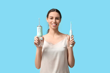 Beautiful young woman with oral irrigator and electric toothbrush on blue background