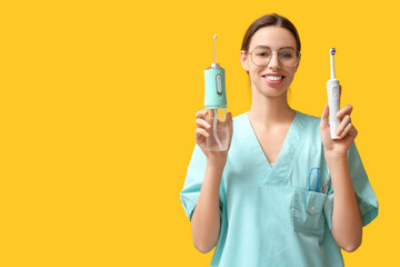 Female dentist with oral irrigator and electric toothbrush on yellow background