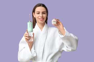 Beautiful young woman with oral irrigator and dental floss on lilac background