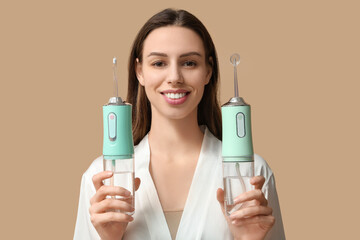 Beautiful young woman with oral irrigators on brown background