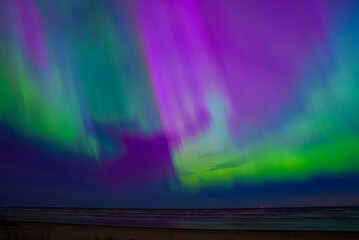 Stunning display of the Aurora Borealis with vibrant green, purple, and blue hues over the calm sea...
