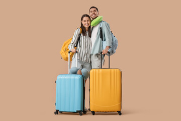 Beautiful young happy couple of tourists with suitcases, backpacks and travel pillows on brown background