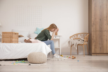 Tired young mother resting in bedroom with scattered toys on floor