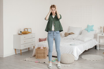 Tired young mother in bedroom with scattered toys on floor