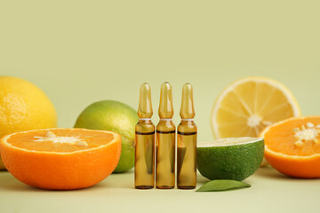 Ampules with vitamin C and fresh citrus fruits on color background